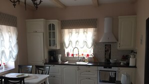Une cuisine avec des meubles blancs, une table  à manger avec des chaises, une fenêtre avec des rideaux et une cuisinière.