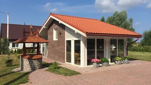 Une maison à deux étages, avec un toit recouvert de tuiles rouges, une façade en briques et un porche abrité orné de plantes en pot.
