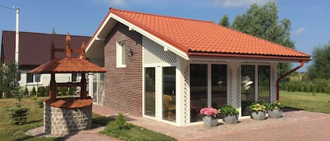 A two-story house with a red-tiled roof, a brick exterior, and a covered porch with potted plants.