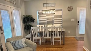 A living room with a sofa, a dining area with chairs and a table, a patterned rug, and a ceiling fan. - Ocean Views All Decks - 4BR/3BA Stilt Home in Ocean Lakes - 1006 w Golf Cart Opt (Myrtle Beach)