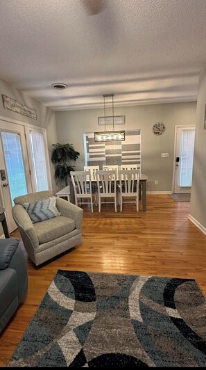 A living room with a sofa, a dining area with chairs and a table, a patterned rug, and a ceiling fan.