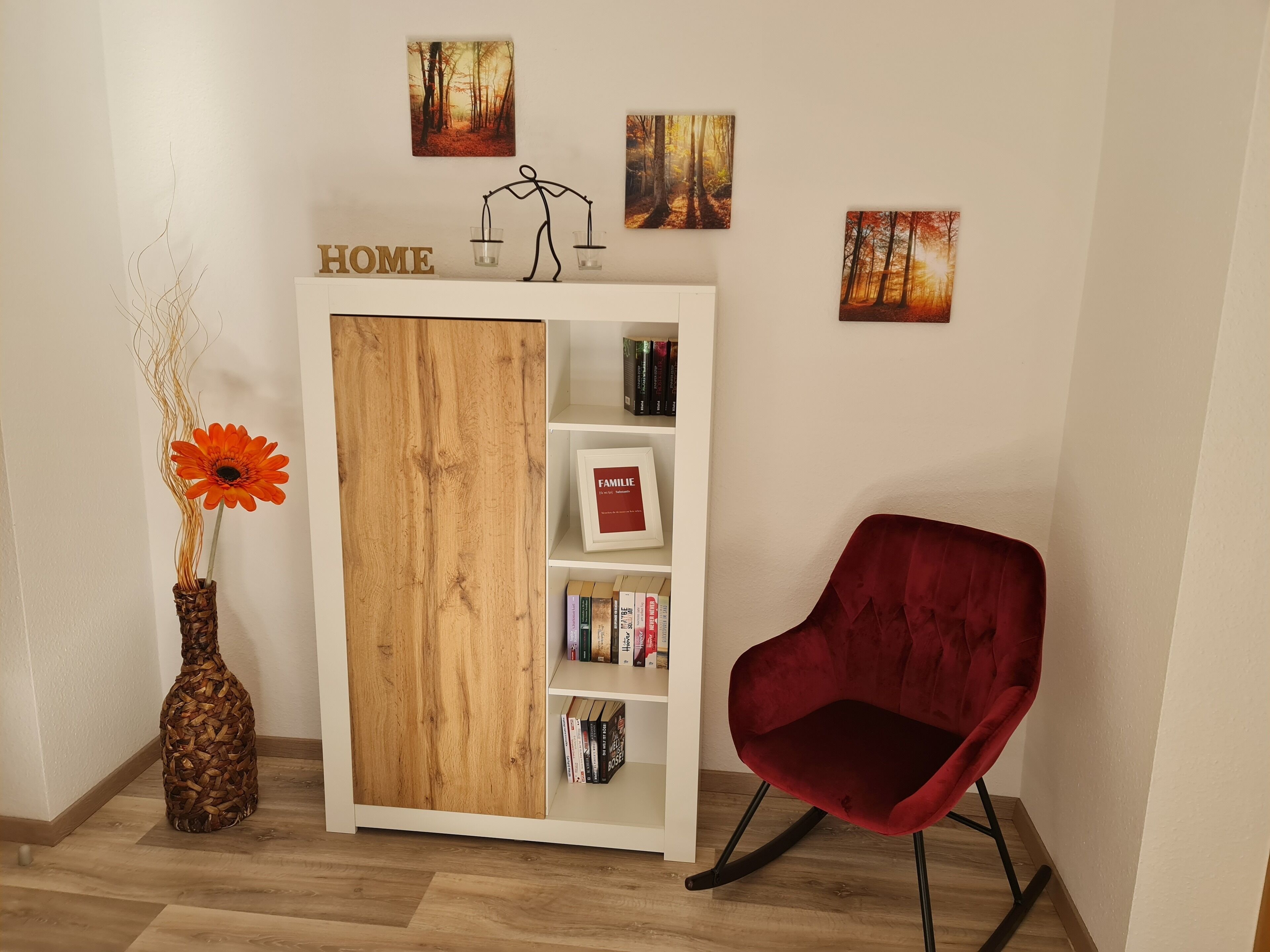 A room with a wooden bookshelf, a red chair, and a vase with a flower.