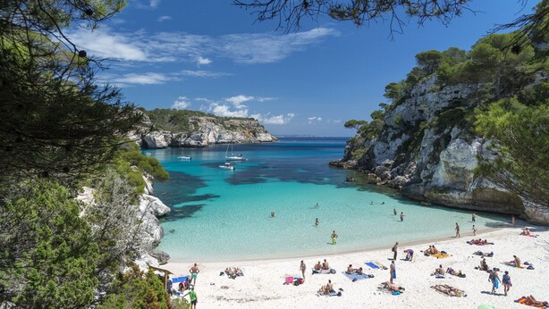 Une plage aux eaux turquoise et limpides, bordée de falaises rocheuses et d’une végétation luxuriante.