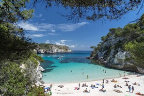 A beach with clear turquoise waters, rocky cliffs, and lush greenery. - Charming villa, private pool 97m2, WIFI, 8 minutes walking beach (SANT LLUIS)