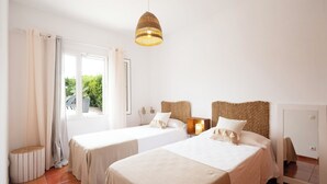Une chambre d’hôtel avec deux lits, une grande fenêtre avec des rideaux, une tête de lit en osier et un luminaire suspendu.