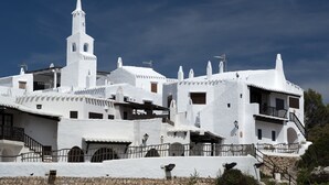 Un bâtiment blanc doté d’un clocher et de nombreuses fenêtres, entouré d’un mur de pierre et d’une clôture en bois.