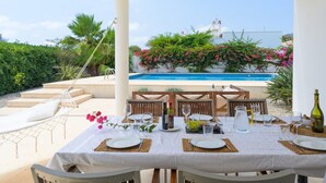 Un espace de restauration en plein air avec vue sur la piscine, des nappes blanches et un hamac.