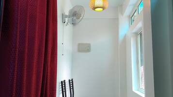Ein schmaler Flur mit rotem Vorhang, einem Wandventilator, einem kleinen Tisch und einem Fenster.