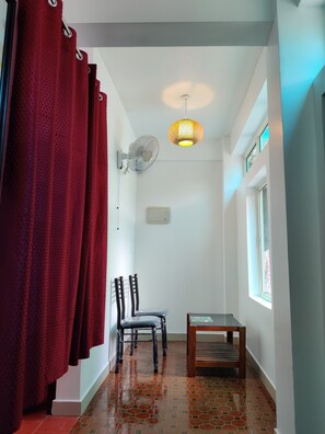 A narrow hallway with a red curtain, a wall-mounted fan, a small table, and a window. - woodrose resort (Vythiri)
