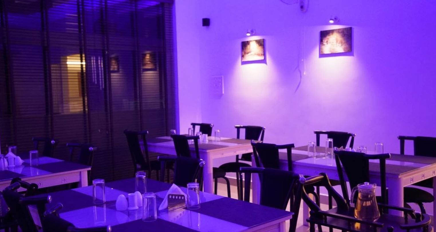 A restaurant with tables and chairs, purple lighting, and wall-mounted picture frames.
