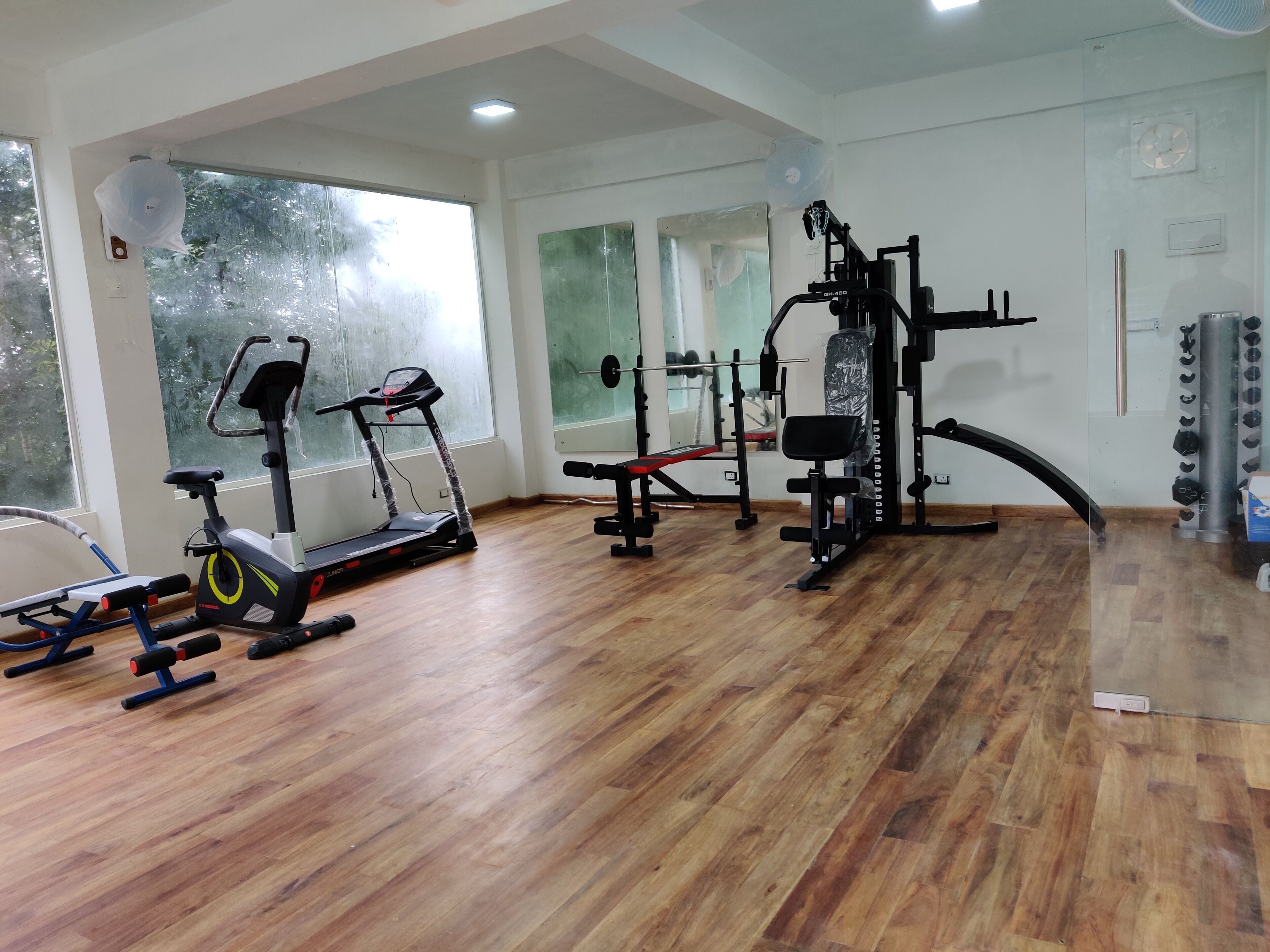 A gym with exercise equipment, wooden flooring, and large windows.