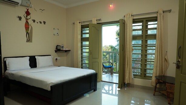 A bedroom with a bed, a chair, and a balcony with a view. - woodrose resort (Vythiri)