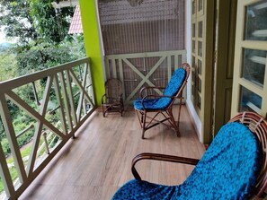 A balcony with a wooden floor, two wicker chairs with blue cushions, and a view of greenery. - woodrose resort (Vythiri)