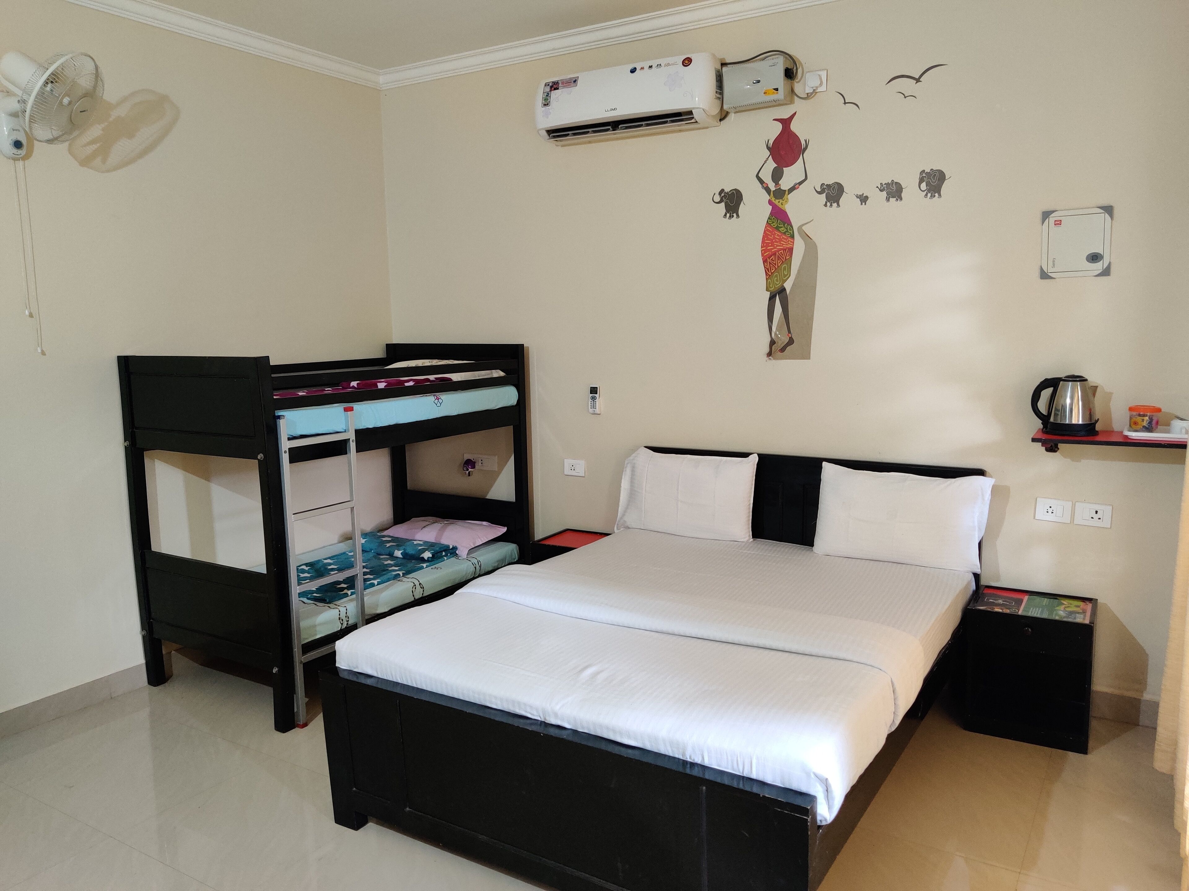 Una habitación con una cama individual, una litera, aire acondicionado, un estante con hervidor y una decoración en la pared.