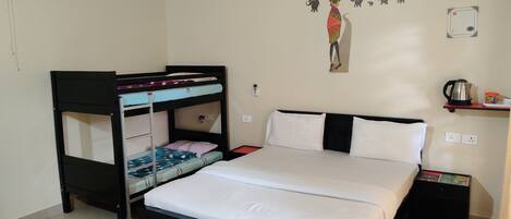 Una habitación con una cama individual, una litera, aire acondicionado, un estante con hervidor y una decoración en la pared.