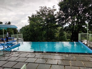 A swimming pool with a tiled deck, surrounded by trees and a covered seating area. - woodrose resort (Vythiri)