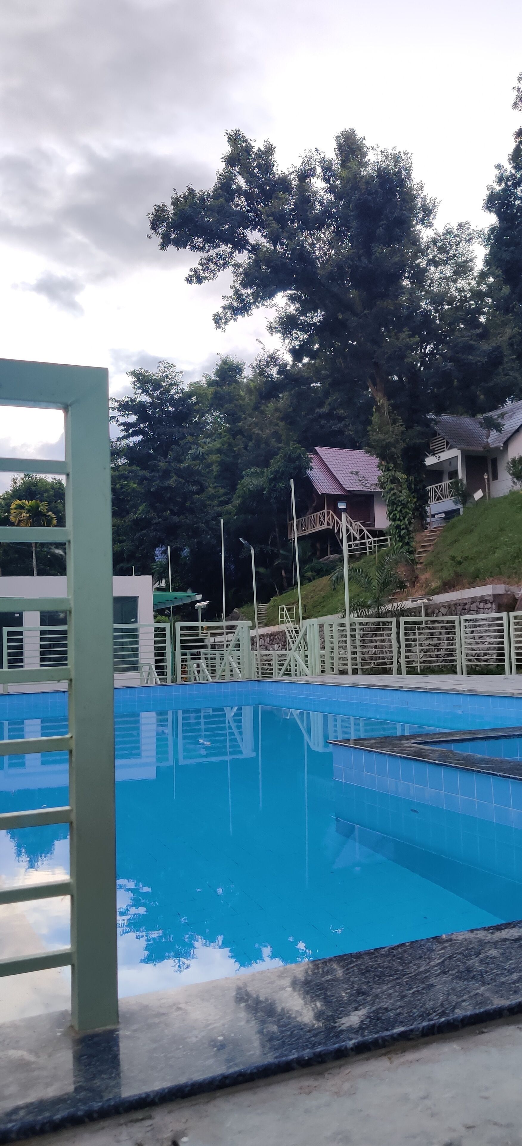 Una piscina con superficie d'acqua cristallina blu, circondata da una recinzione bianca e una struttura metallica verde.