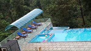 Una piscina en la azotea con sillones azules y una cubierta de vidrio.