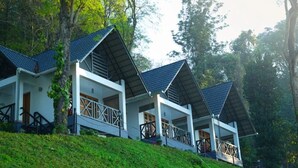 Una hilera de cabañas blancas con techos oscuros, ubicadas en una ladera con vegetación exuberante.