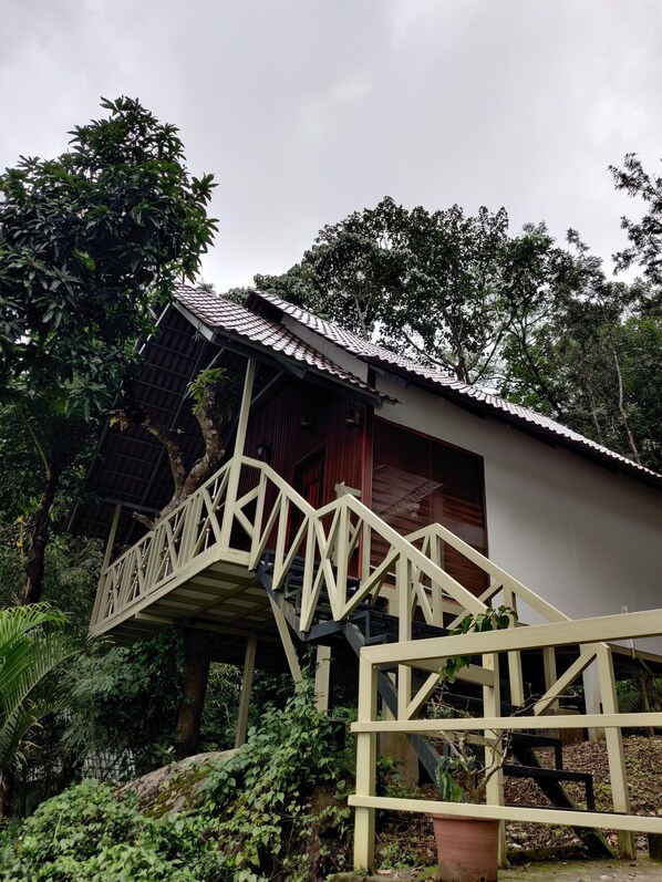 A wooden staircase leading to a building with a tiled roof, surrounded by lush greenery. - woodrose resort (Vythiri)