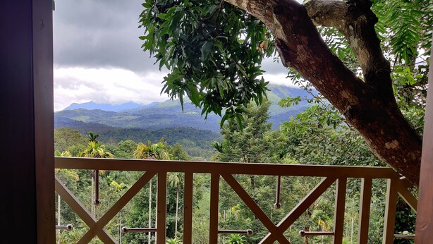 Un balcón de madera con vistas a montañas verdes y un cielo nublado.