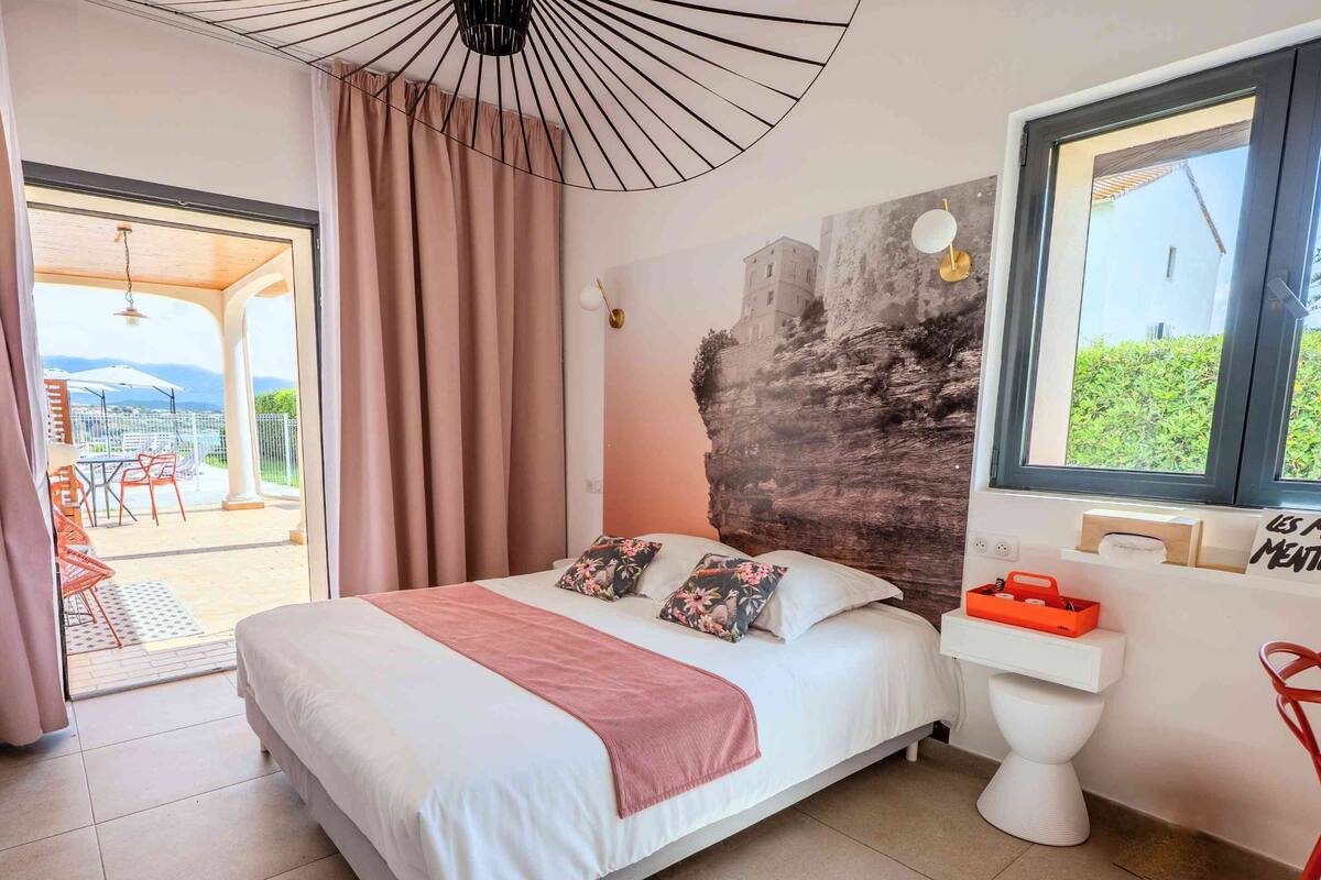 A bedroom with a bed, a window, a toilet, and a view of the outdoors.