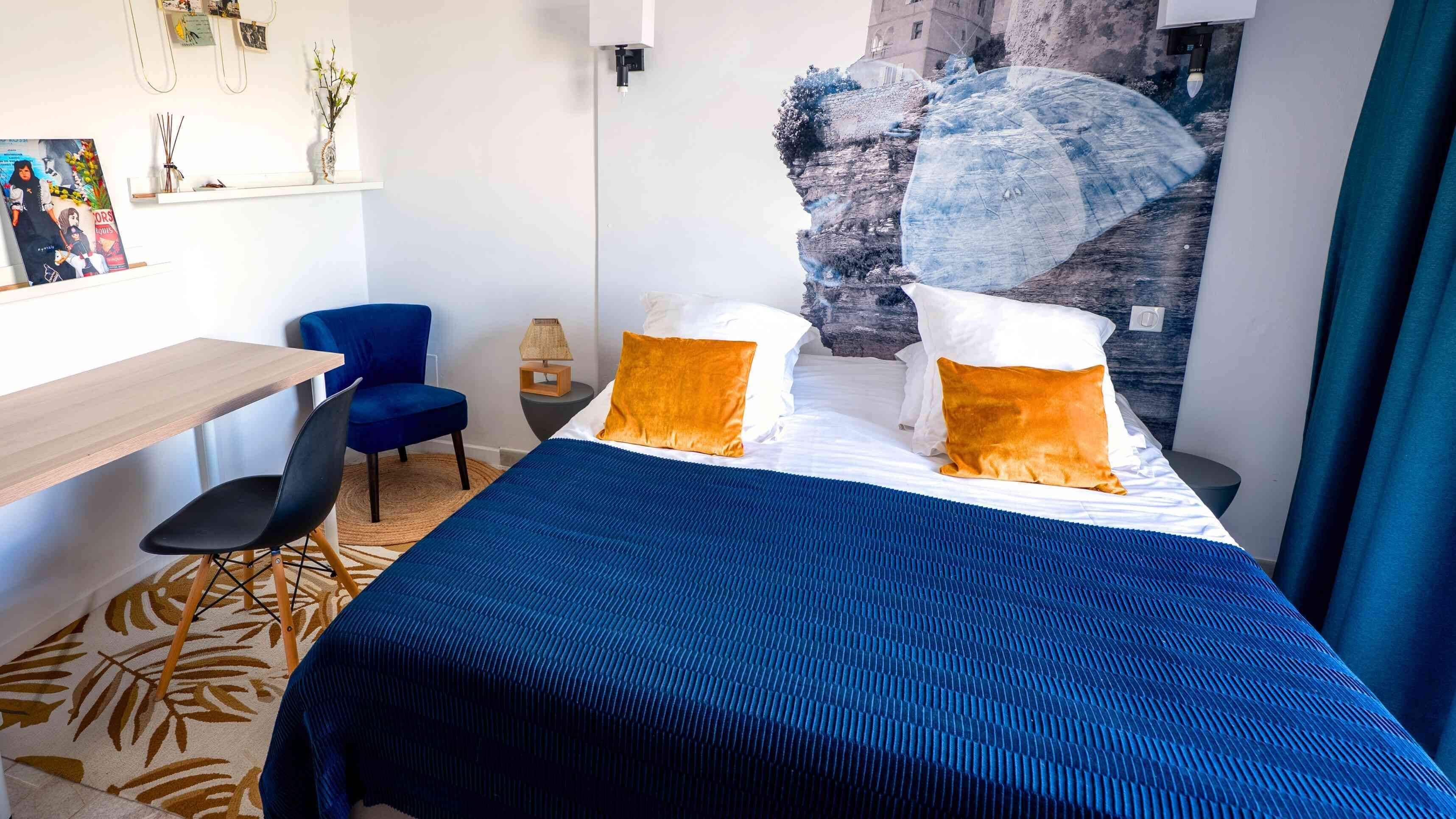 A hotel room with a bed, a desk, a chair, and a wall with a large abstract painting.