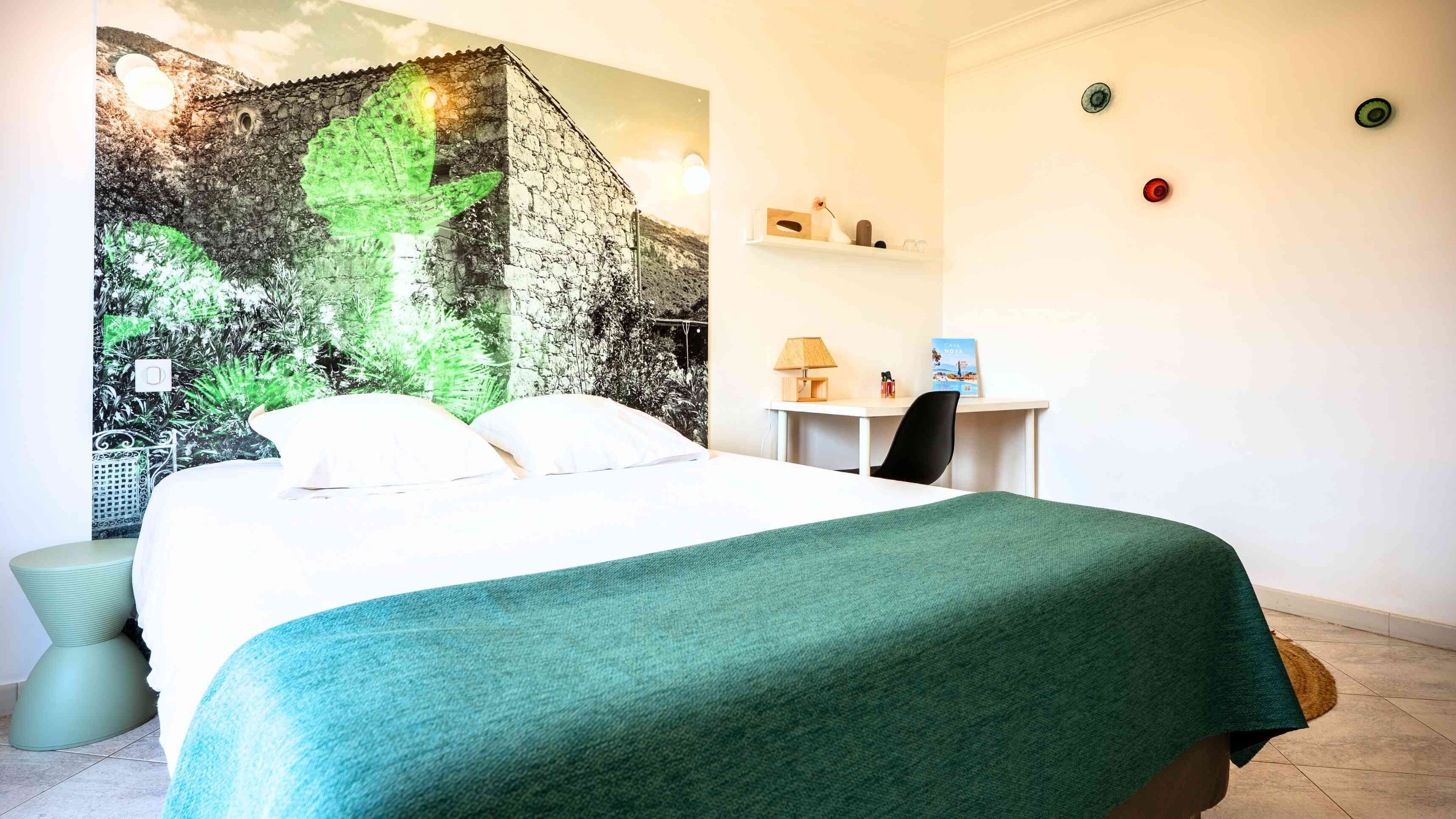 A bedroom with a bed, a desk, and a wall with a green leafy pattern.