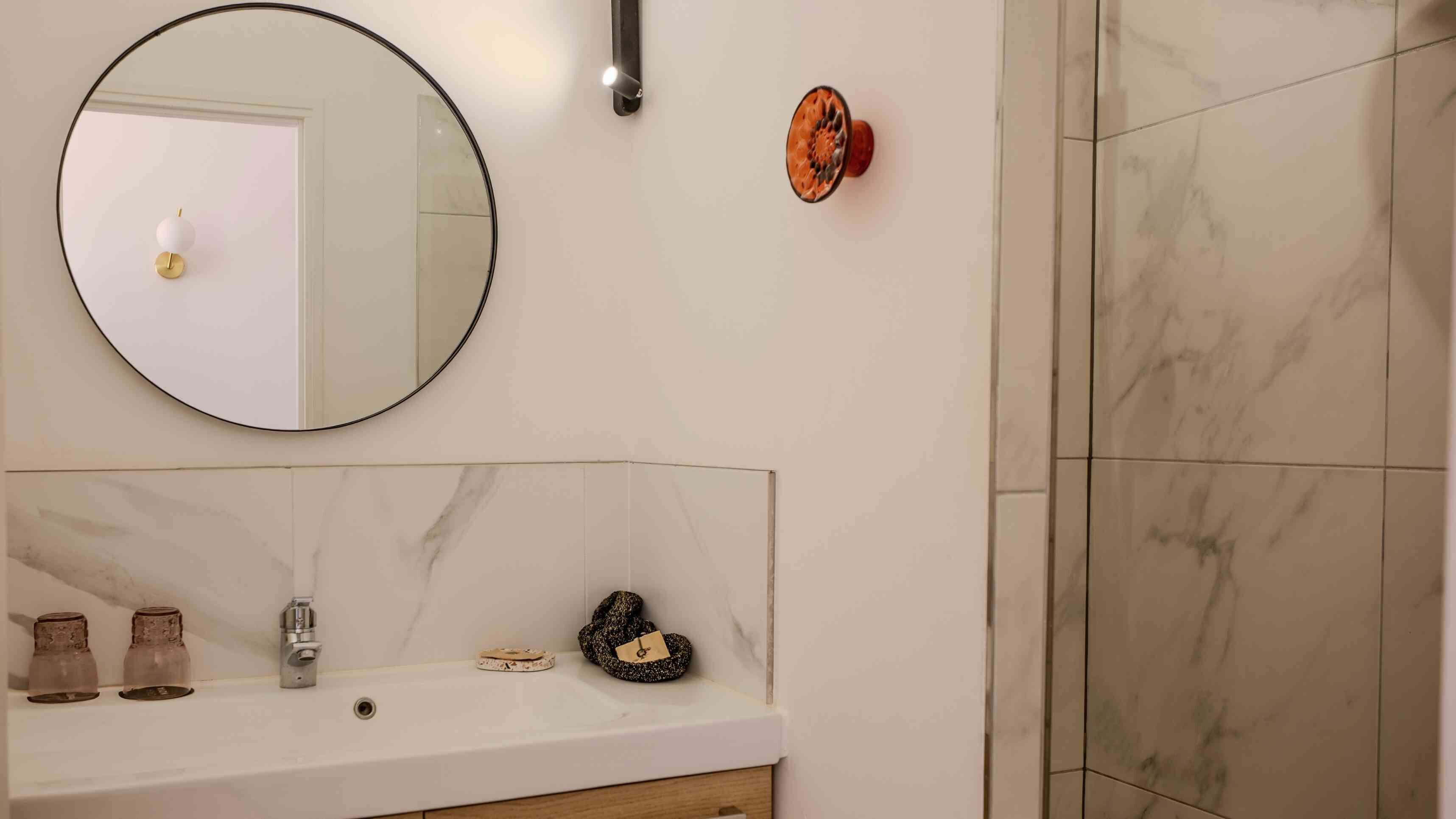 A bathroom with a round mirror, a sink, and a shower area.