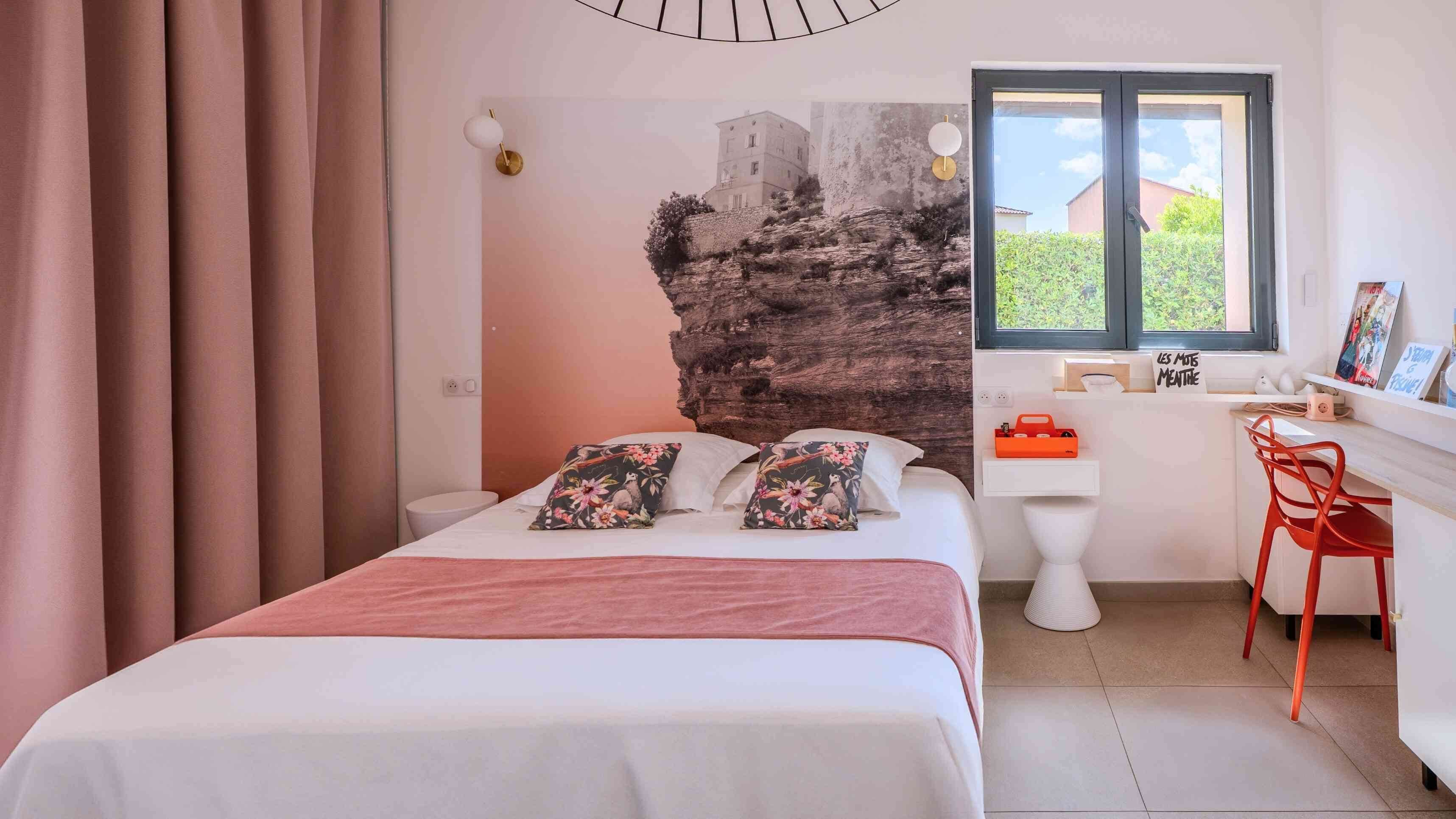 Un dormitorio con cama, escritorio, silla, ventana y pared de textura rocosa.