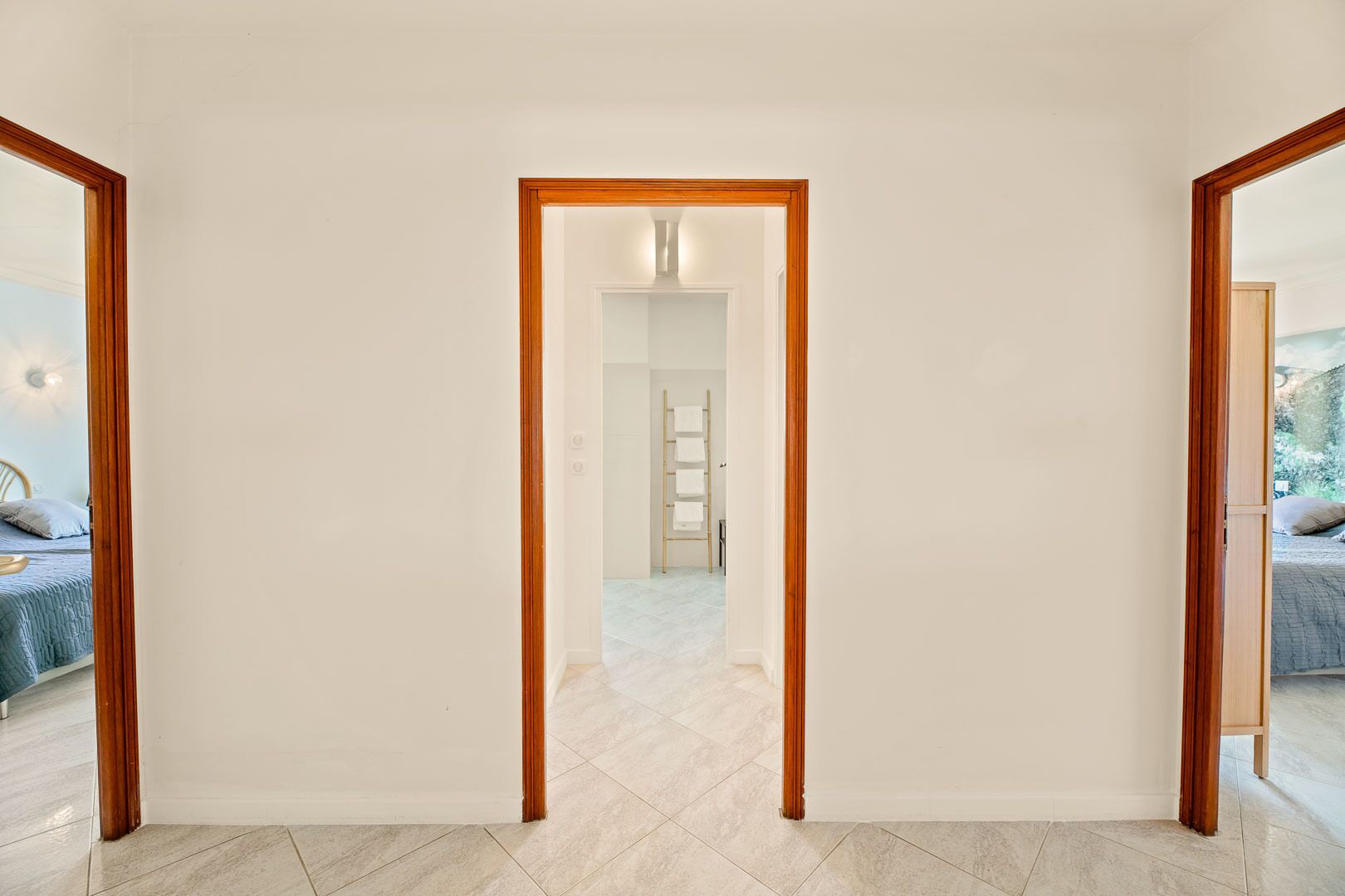 A hallway with a wooden-framed door leading to a bedroom with a bed and a nightstand.
