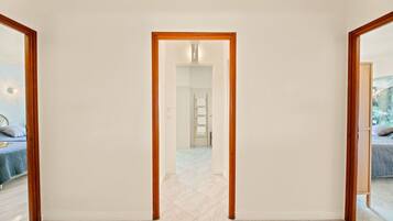A hallway with a wooden-framed door leading to a bedroom with a bed and a nightstand.