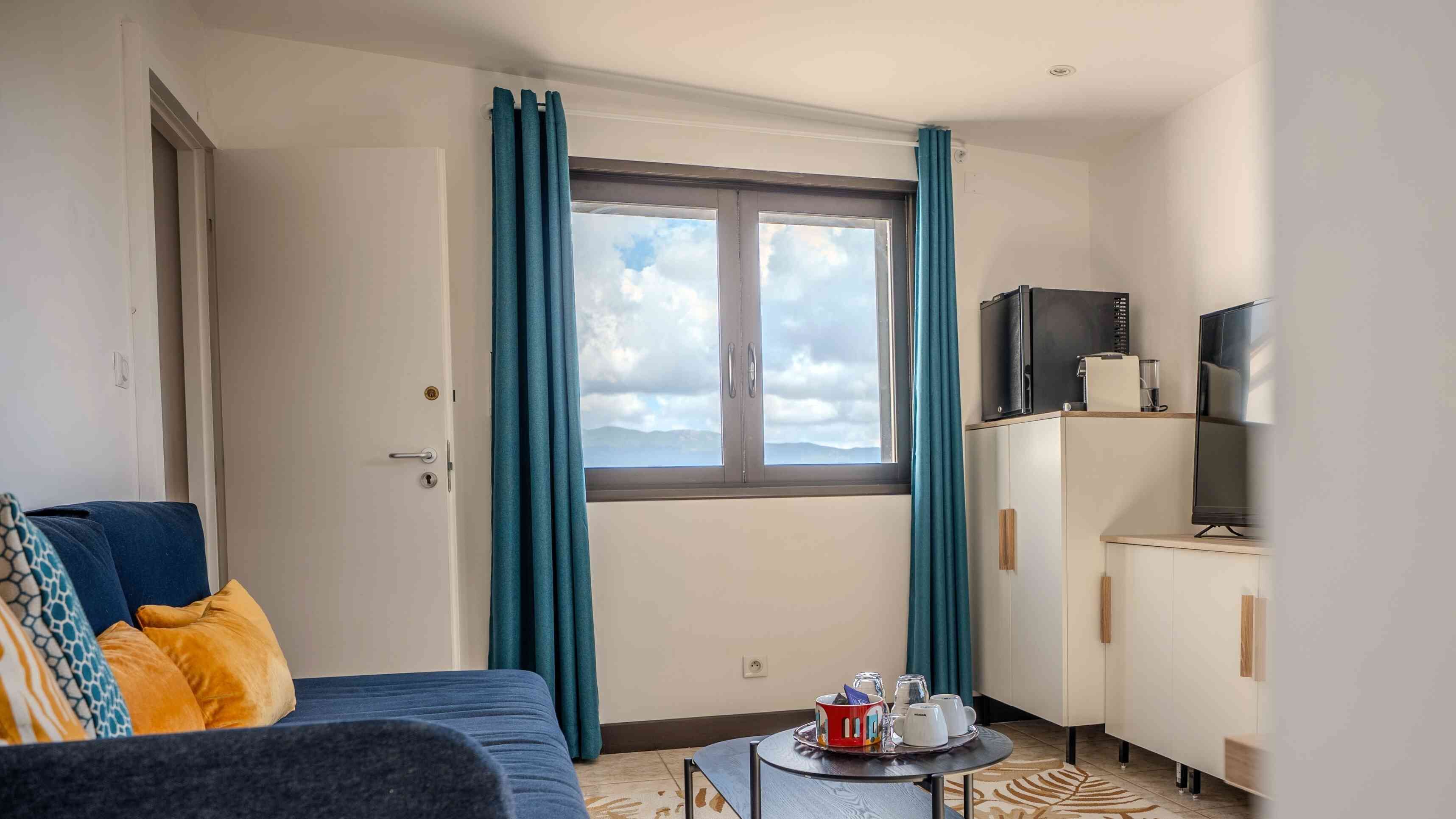 Ett hotellrum med en säng, ett litet bord med koppar och en vattenkokare, en tv och ett fönster med gardiner.