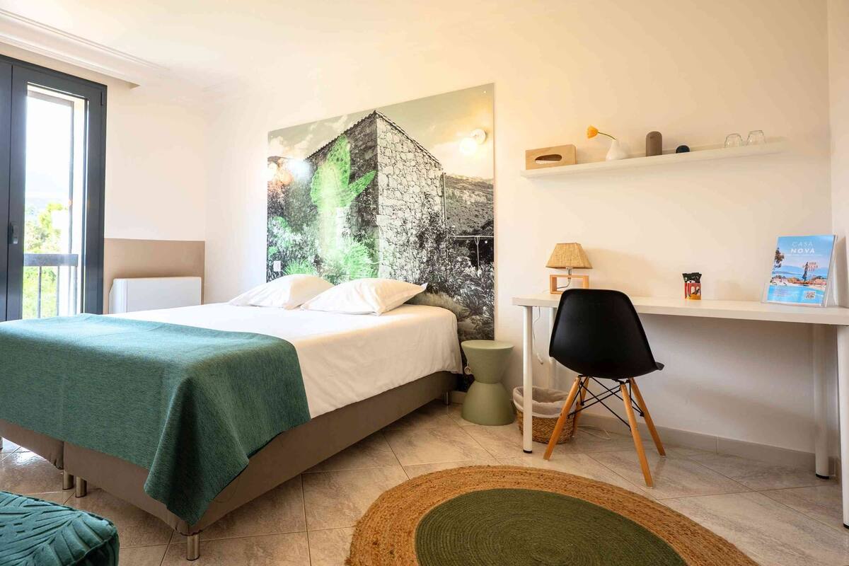 A hotel room with a bed, a desk, a chair, a small rug, and a window with curtains.