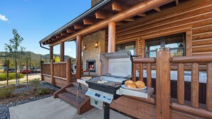 An outdoor grill area with a stone fireplace, wooden deck, and a view of the surrounding landscape. - Chic Retreat – Indoor/Outdoor Fireplace, Private Jacuzzi, Great Location! (Estes Park)