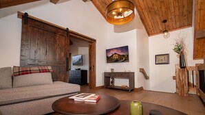 A cozy living room with a wooden ceiling, a sofa, a coffee table, and a painting of a house. - Chic Retreat – Indoor/Outdoor Fireplace, Private Jacuzzi, Great Location! (Estes Park)