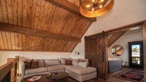 A loft-style room with a wooden ceiling, a large sofa, two round tables, and a view through an open door. - Chic Retreat – Indoor/Outdoor Fireplace, Private Jacuzzi, Great Location! (Estes Park)