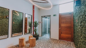 Een moderne lobby met een mozaïekvloer, houten krukken, een potplant en een houten deur.