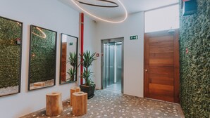 Een moderne lobby met een mozaïekvloer, houten krukken, een potplant en een houten deur.