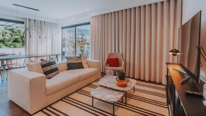 Een moderne woonkamer met een bank, fauteuil en salontafel. Achtergrond toont een eethoek met een tafel en stoelen.