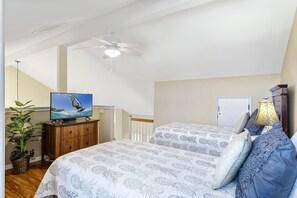 Ein Schlafzimmer mit zwei Betten, einem Deckenventilator, einem Fernseher auf einer Holzkommode und einer Topfpflanze.