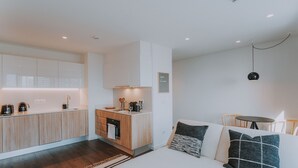 A modern, well-lit room with a kitchen area, a sofa with cushions, and a small table. - FLH Casa Branca Madeira 301 (Funchal)