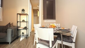 A compact living space with a dining area featuring a round glass table, white chairs, and a small bookshelf with a lit lantern. - The Sants's balcony (Barcelona)