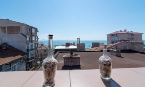 Two glass bottles with seashells on a rooftop terrace overlooking a coastal cityscape.