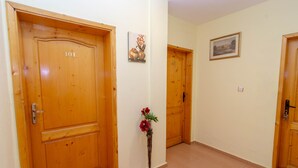 A hallway with wooden doors, numbered 101 and 102, and a small vase with flowers on a stand. - Guest House Fener (Pomorie)