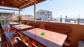 An outdoor seating area with wooden tables and benches, overlooking a cityscape and the sea. - Guest House Fener (Pomorie)