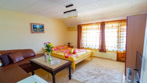 A hotel room with a bed, a sofa, a small table with a vase, and a painting on the wall. - Guest House Fener (Pomorie)