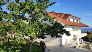 A two-story house with a red-tiled roof, a stone wall, and a paved courtyard.