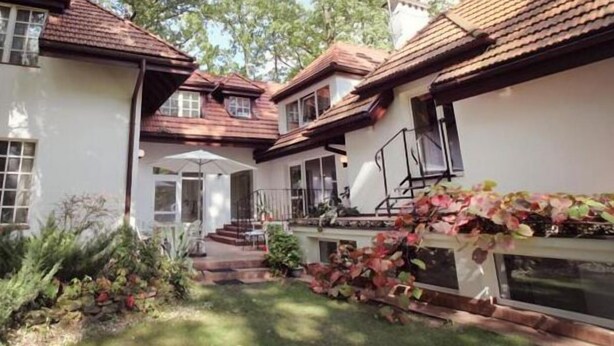 A two-story house with a garden, a covered patio, and a staircase leading to the entrance.