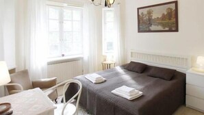 A hotel room with a bed, a chair, a table, and a painting on the wall.